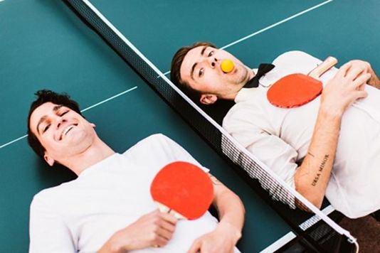 Two people relaxing on a table tennis table with paddles